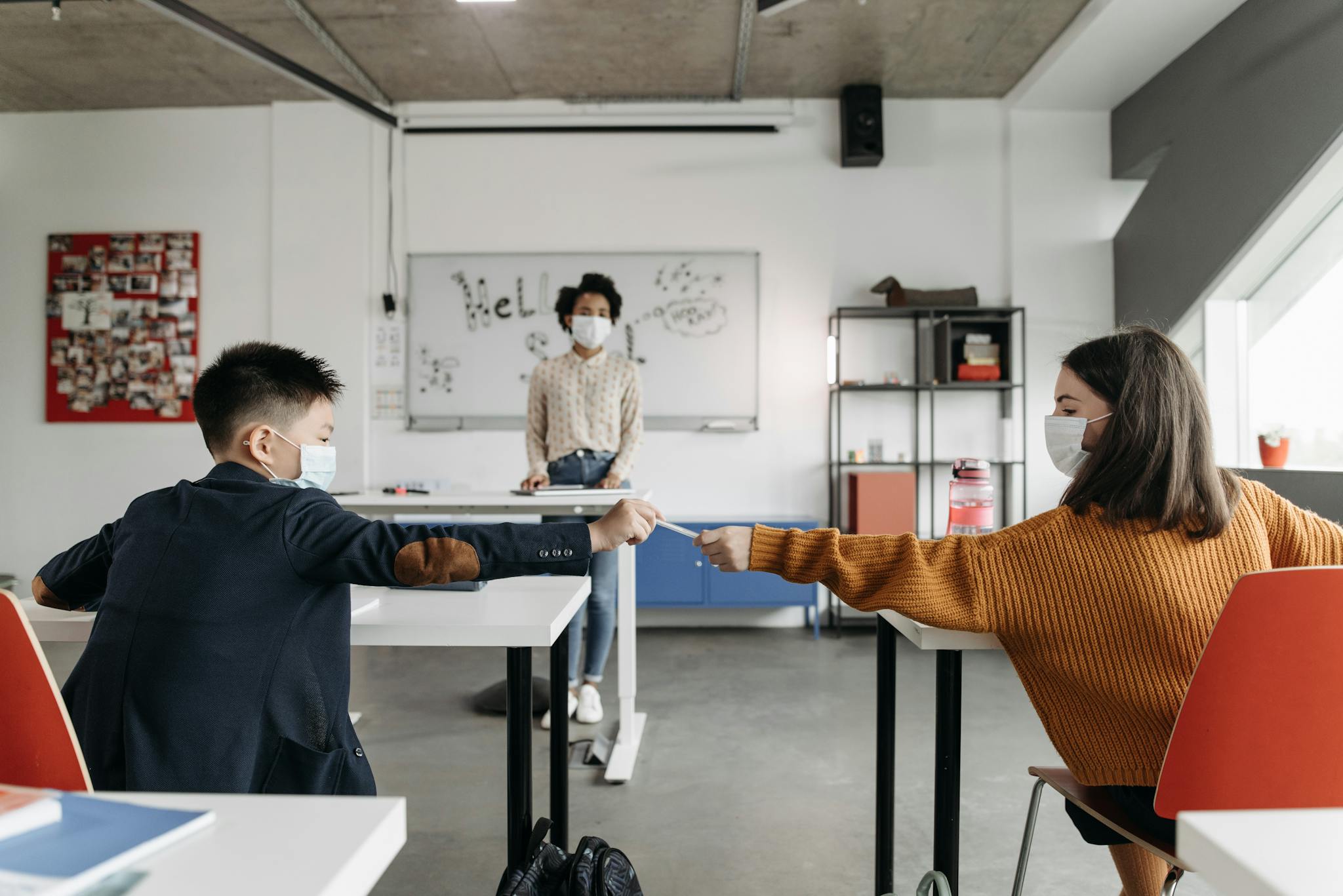 Masked students fist bump in a classroom, symbolizing post-pandemic school resilience.